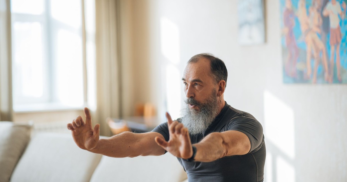 A senior man stretches in a bright living room, embracing fitness and positive aging.