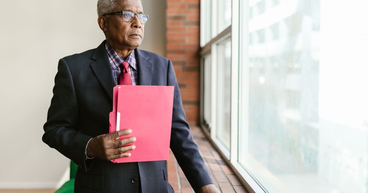 Mature man in suit and glasses holding a folder, gazing out the window.