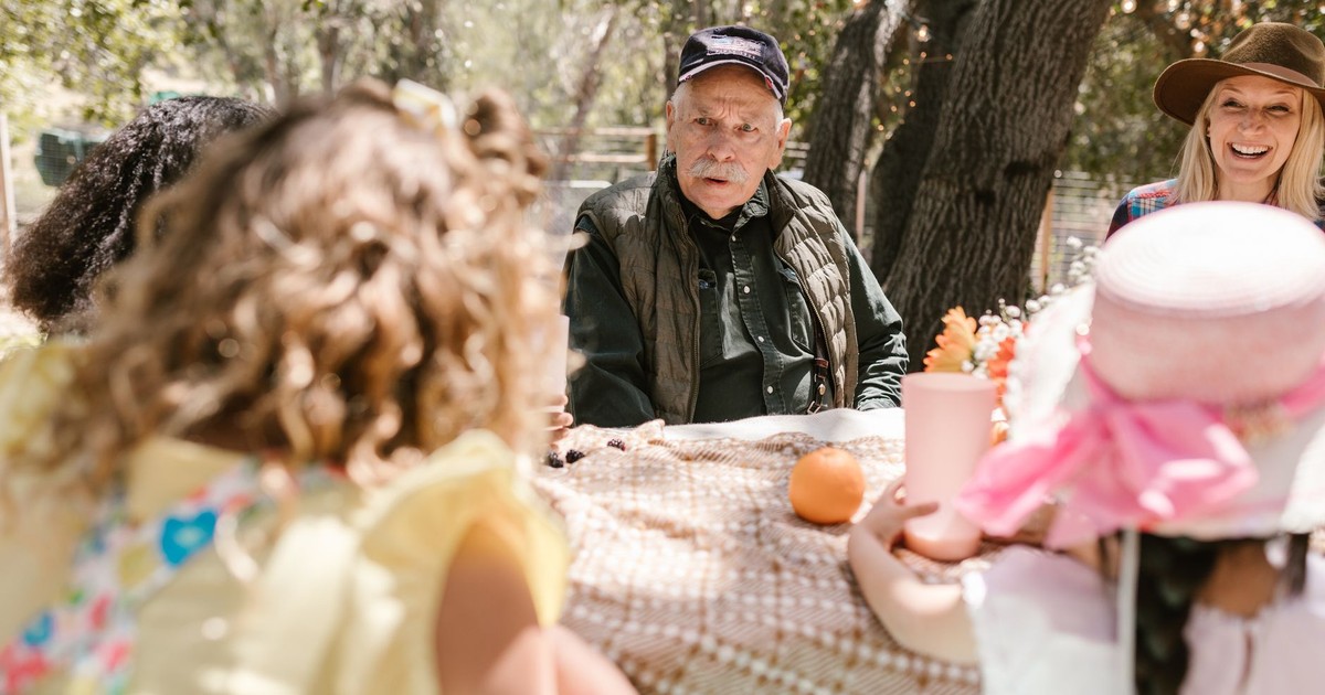 A family enjoys a sunny outdoor gathering, seated around a table with laughter and conversation.