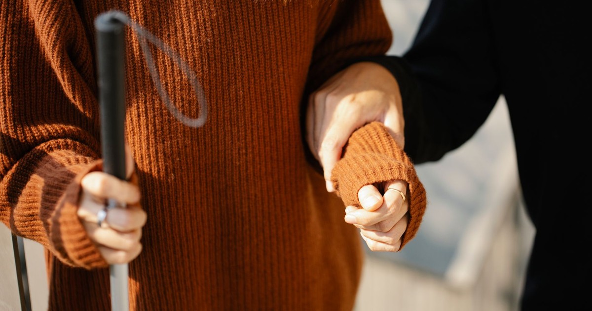 Close-up of two people holding hands, one with a walking cane symbolizing support and visual aid.