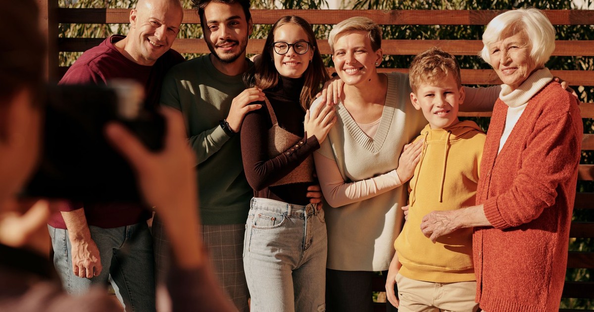 A joyful family portrait featuring multiple generations smiling outdoors in daylight.