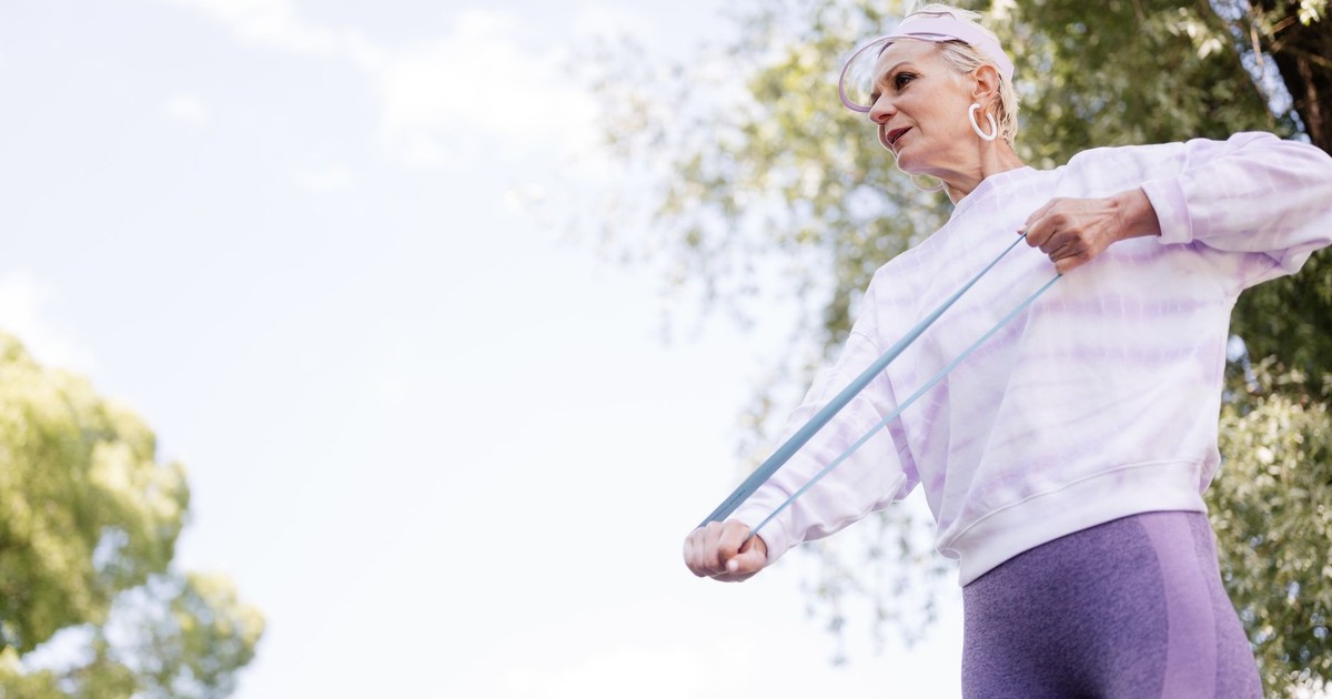 Elderly woman stretching with a resistance band outdoors, promoting senior fitness.