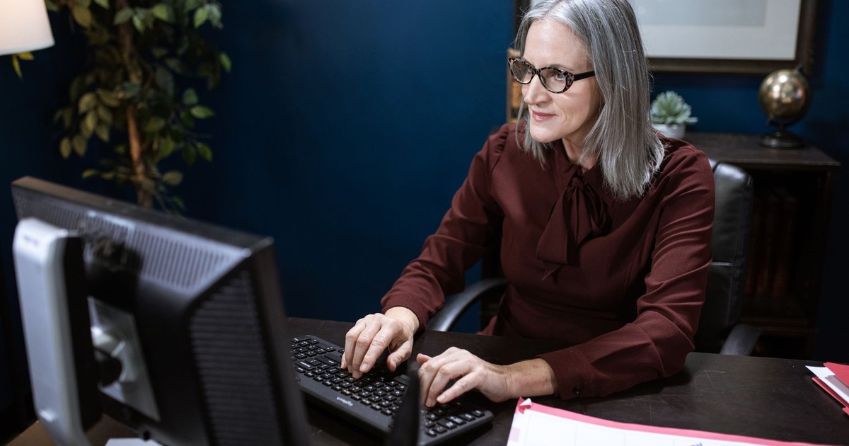 Elderly woman working on a computer in a modern office setting, focused and engaged.