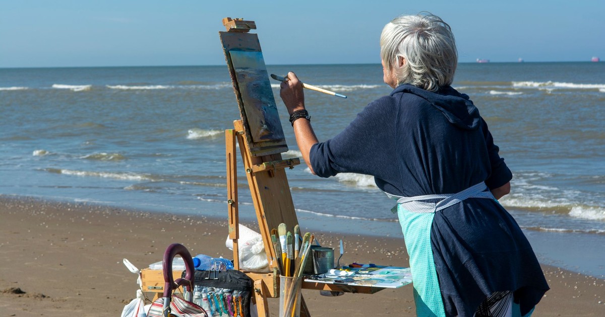 Senior woman artist painting on a beach during summer. Creative outdoor art.