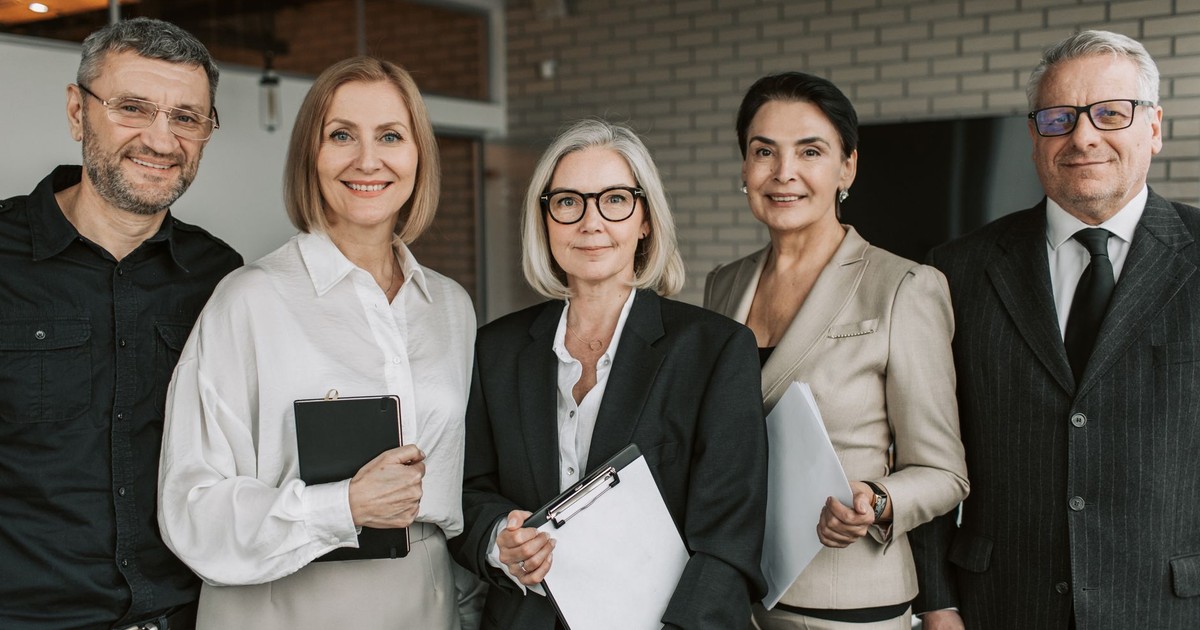 A diverse team of senior business professionals posing confidently indoors.