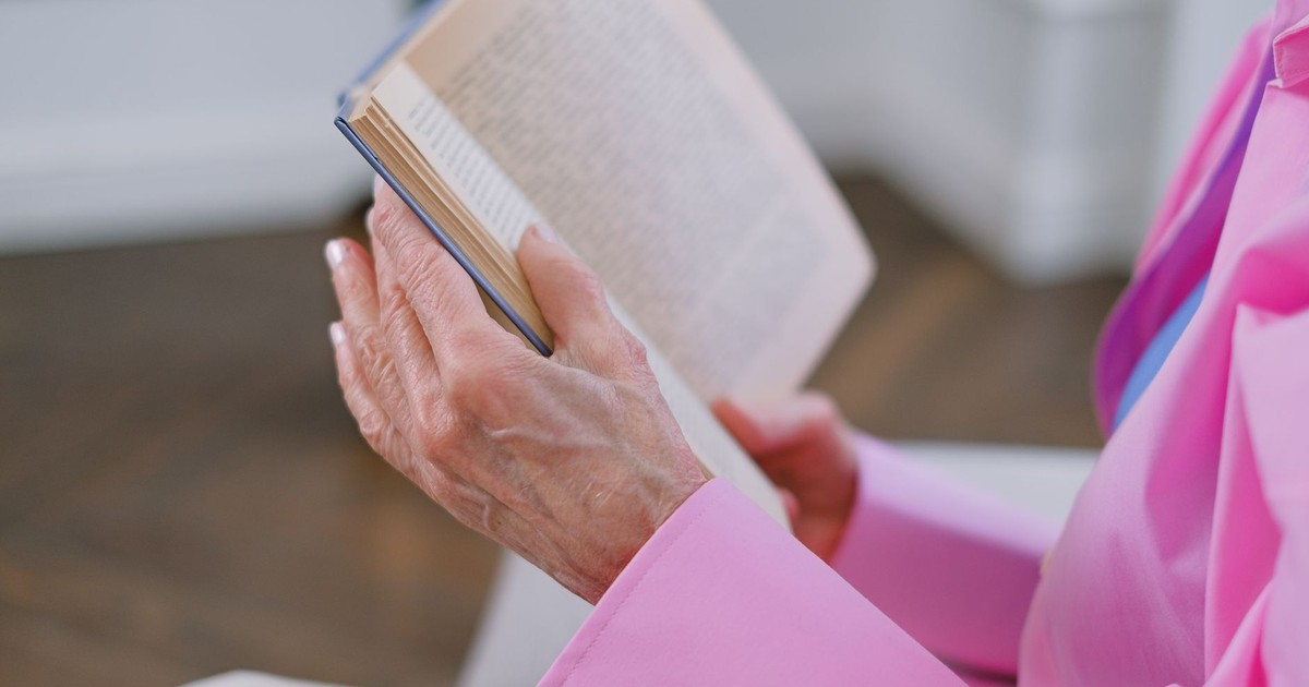 An elderly person leisurely reading a book indoors, showcasing tranquility and focus.