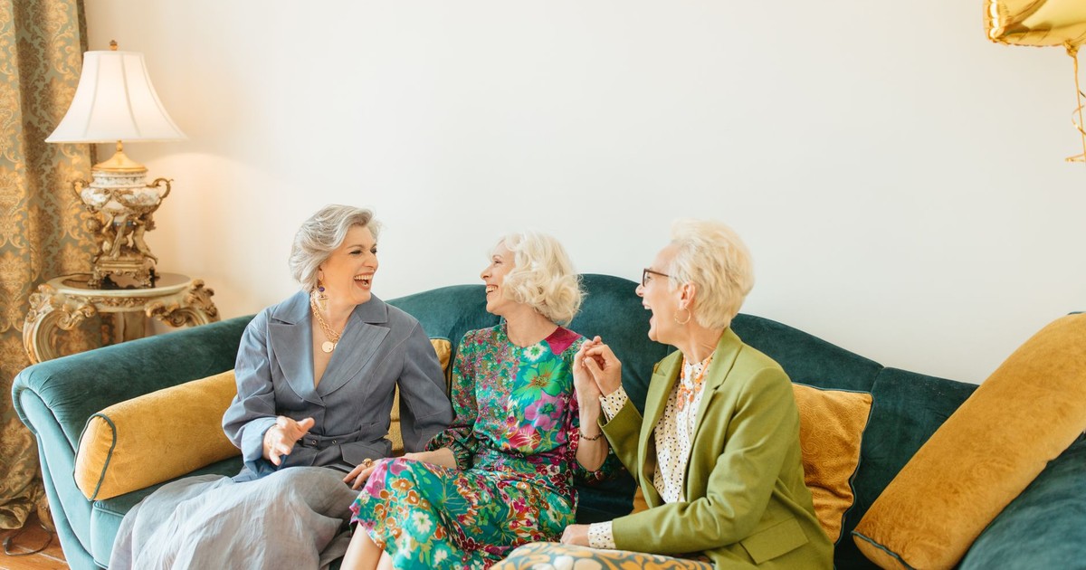 Three elderly women sharing laughter and friendship on a cozy couch indoors.