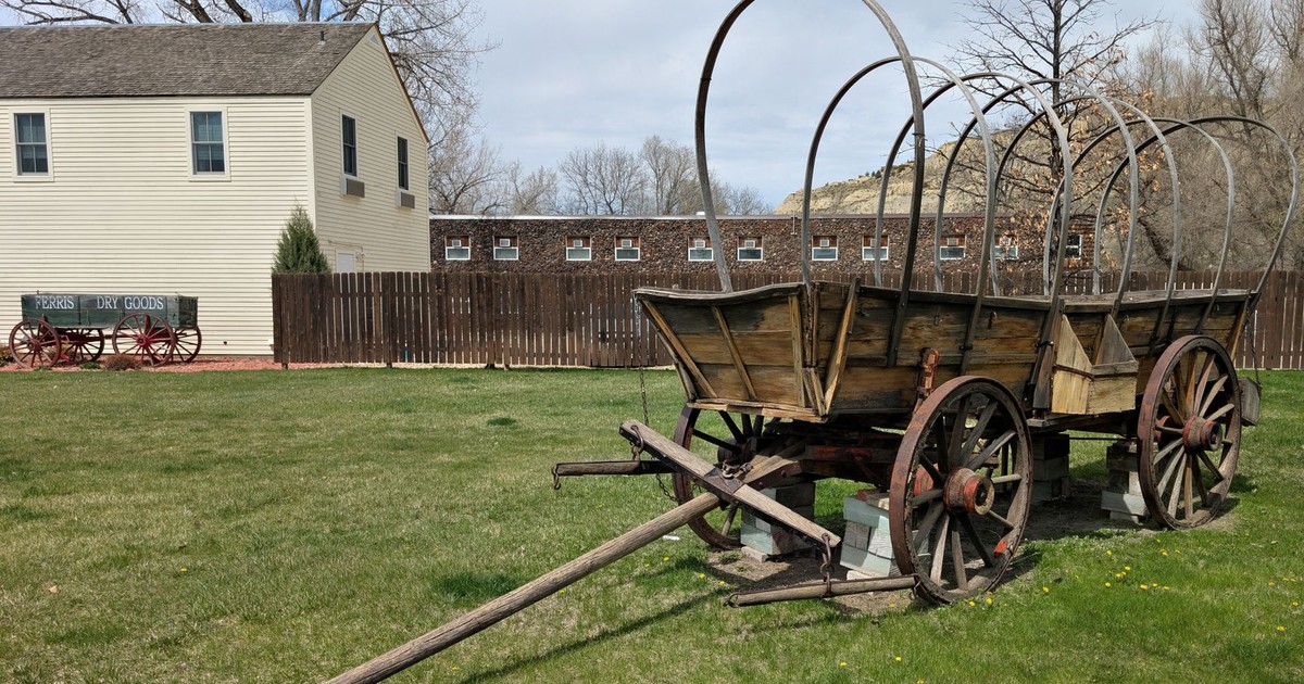 A historical covered wagon displayed in a grassy area near a frontier-style building in Medora.