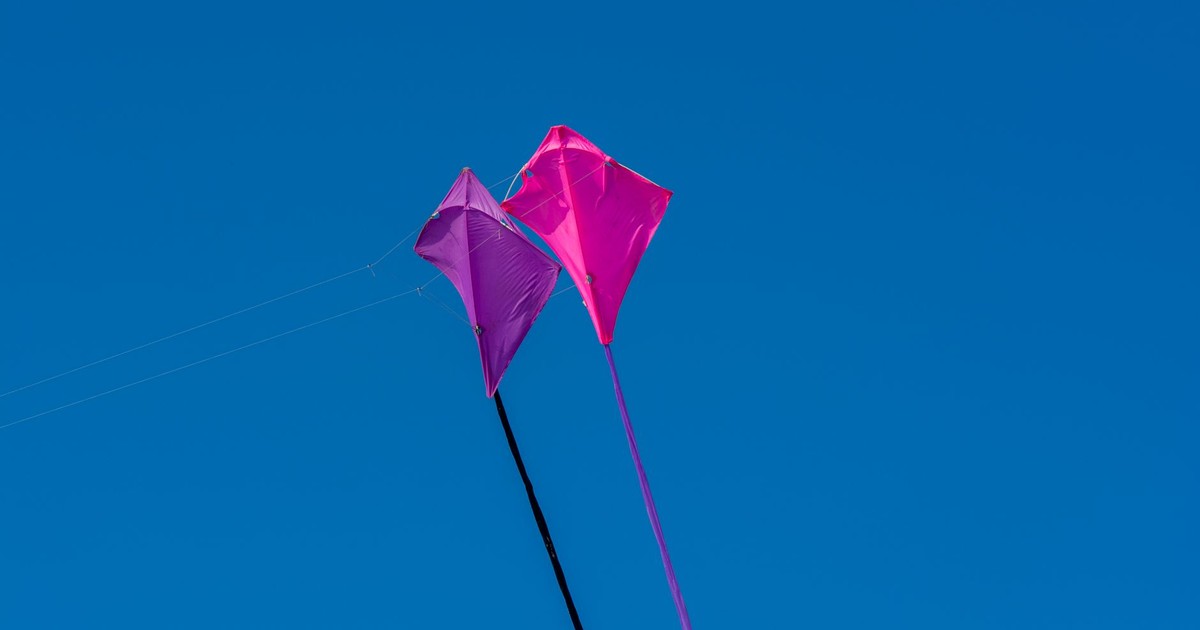 Bright pink and purple kites flying high in a clear blue sky, symbolizing freedom and joy.