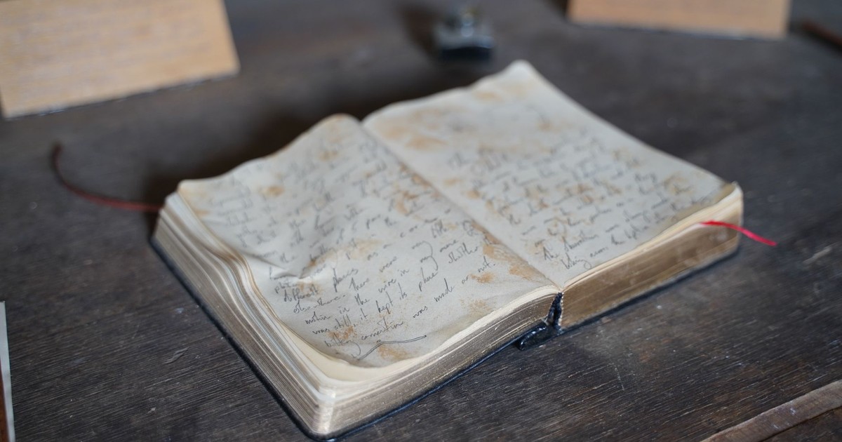 A close-up of an antique open book with handwritten pages on a rustic wooden table.