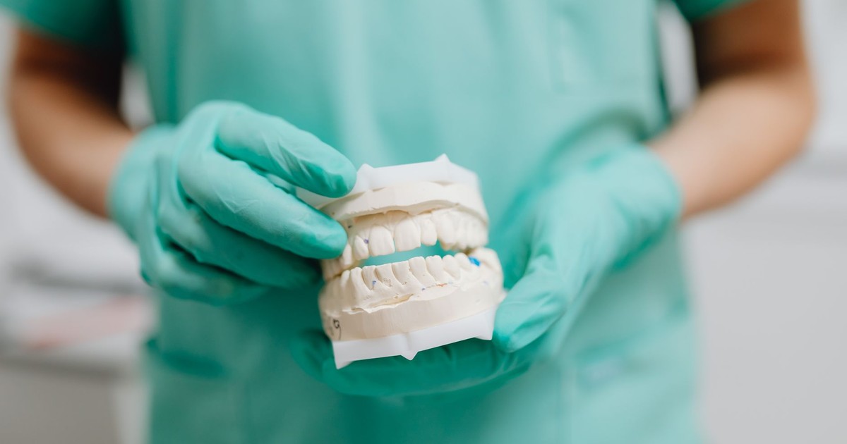 Dentist holding a dental cast with green gloves, representing dental care and prosthetics.