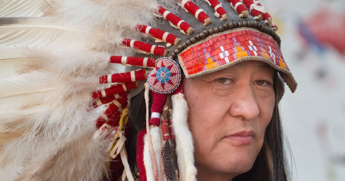 Close-up portrait of a Native American man wearing a traditional feathered headdress.