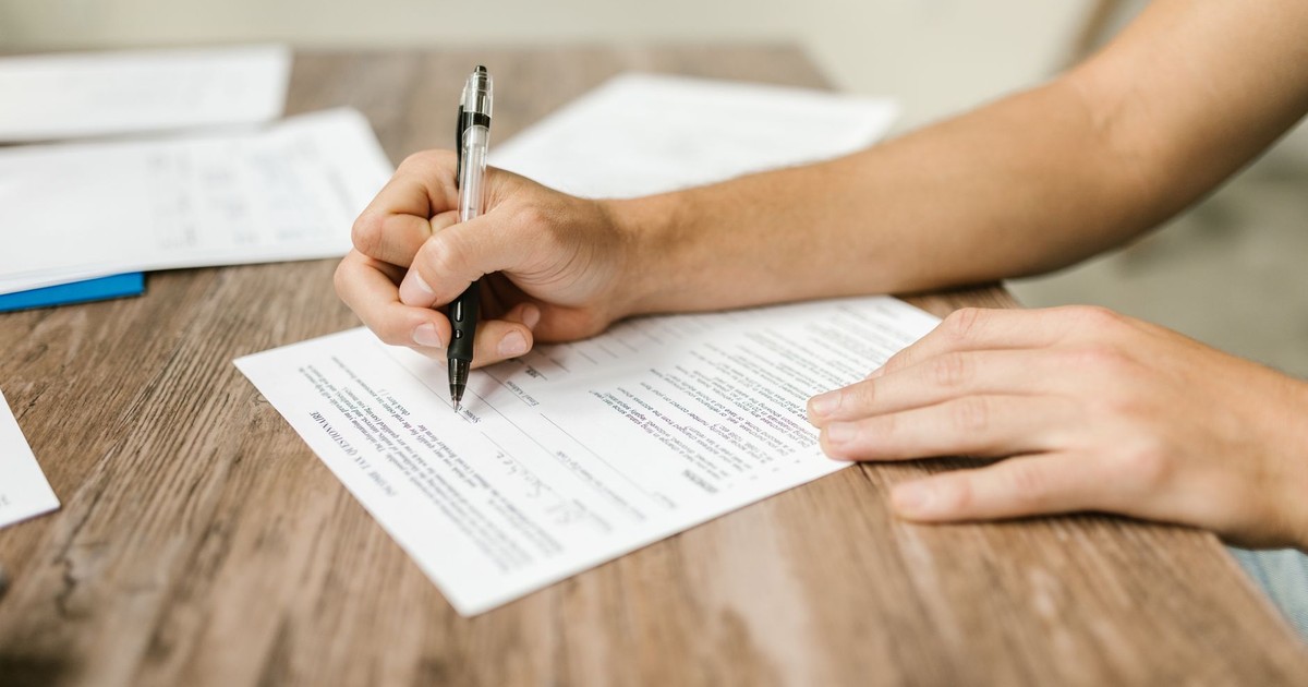 Hand filling out paperwork with a pen, showcasing focus on document completion.