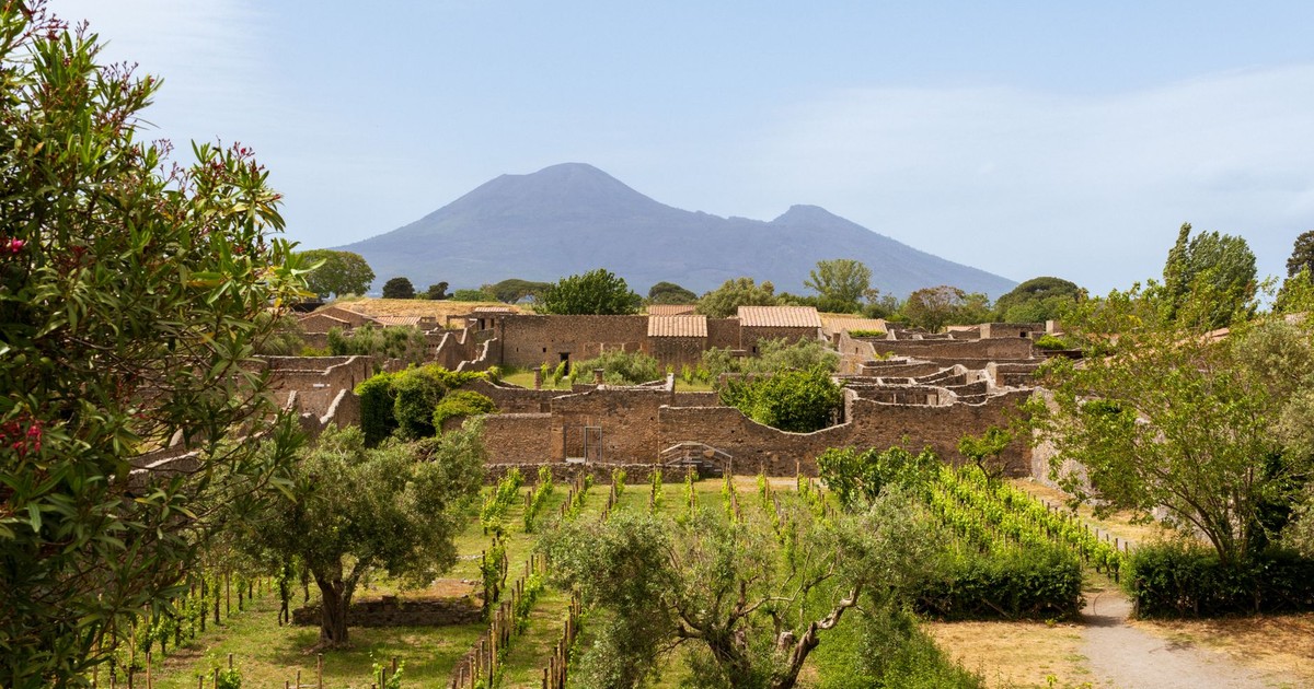 Explore the historic ruins of Pompeii with a stunning view of Mount Vesuvius, set in a lush landscape.