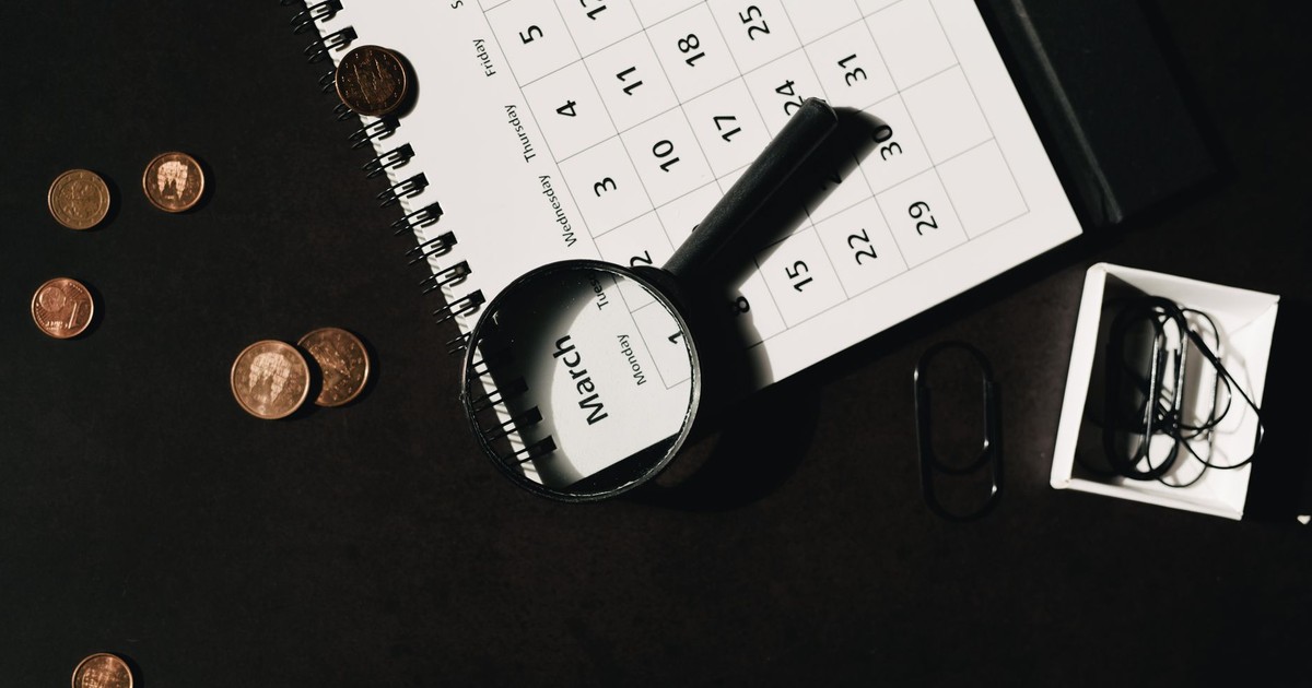 Top view of a calendar with a magnifying glass and coins, ideal for financial themes.