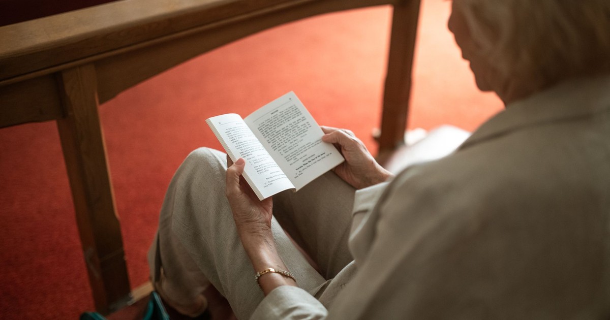 A senior woman reading a religious pamphlet in a church pew, enjoying a moment of peaceful leisure.