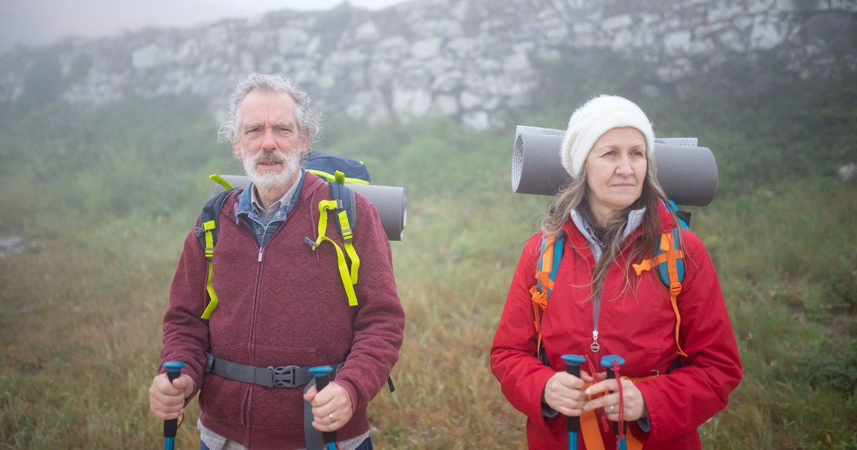 Elderly couple hiking in Portugal with backpacks and trekking poles, embracing adventure.