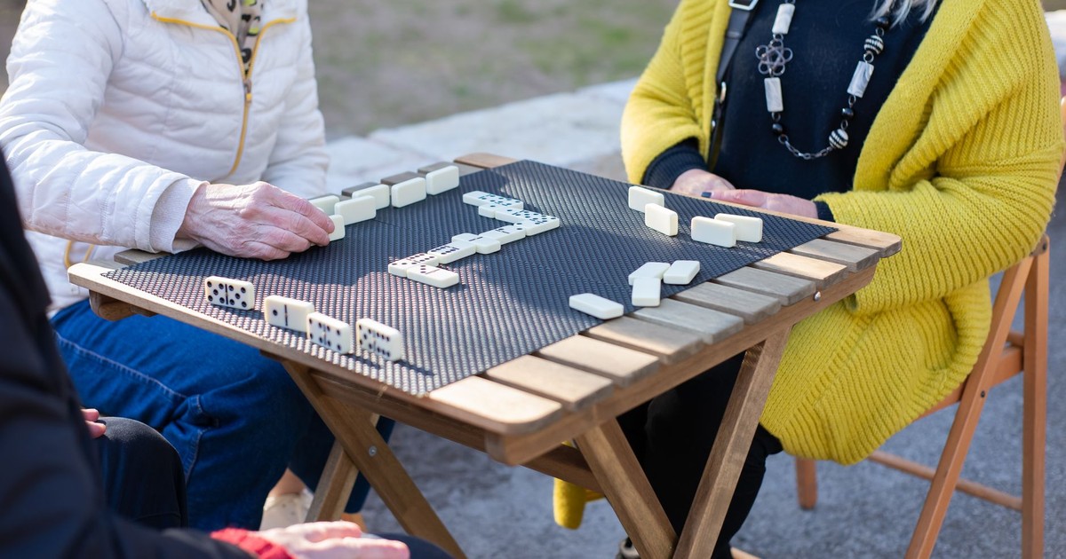 Senior adults playing dominoes at an outdoor table, enjoying leisure time.