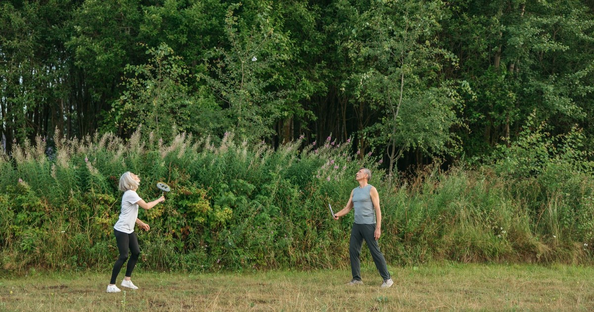 Elderly couple playing badminton outdoors, promoting fitness and togetherness.