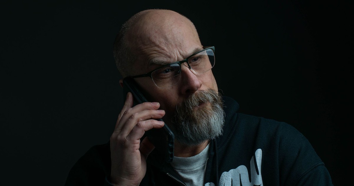 Senior bald man wearing eyeglasses, engages in a phone call against a dark background.