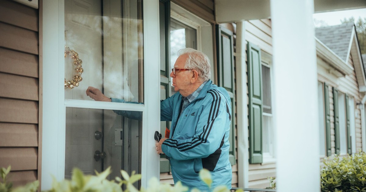 Elderly man in a blue jacket knocking on a suburban house door, showcasing community life.