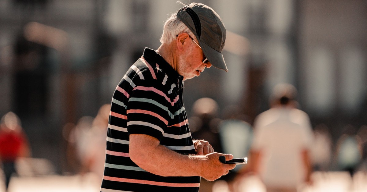 Senior man in striped shirt using smartphone in sunny La Coruña street.