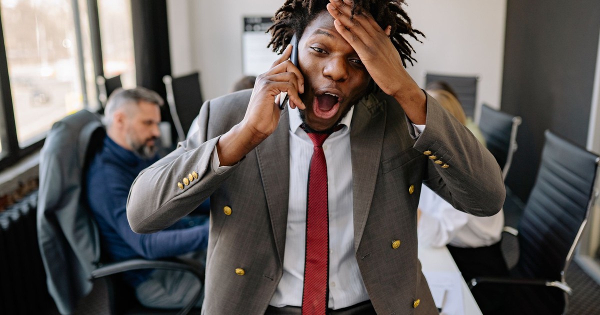A businessman with a surprised expression talks on his phone in an office setting.