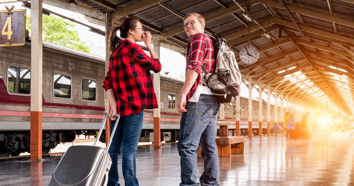 Young couple in a railway station, ready for travel. Bright morning scene with backpacks and luggage.