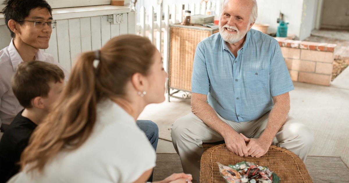 Elderly man enjoying a pleasant family gathering outdoors with diverse group sitting together.