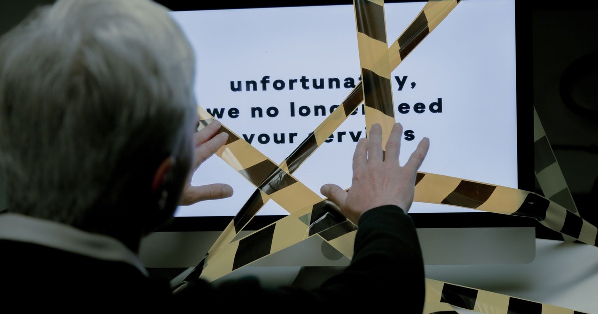 An elderly man reacts to a dismissal message on a computer, conveying ageism and unemployment themes.