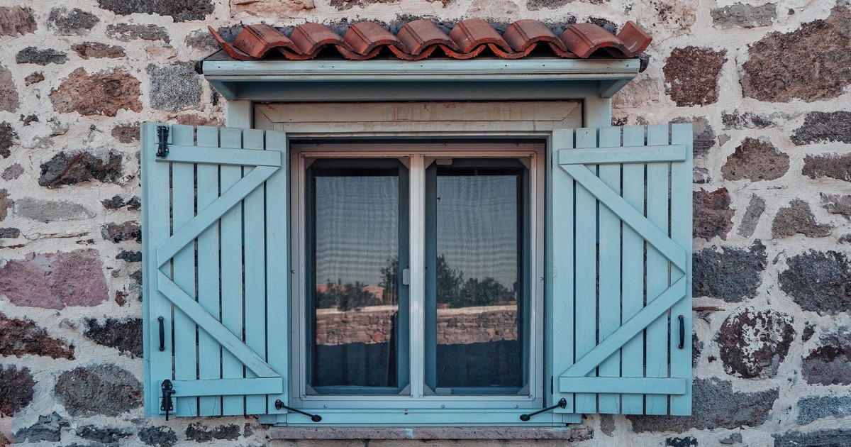 Charming rustic stone house with a blue shuttered window, evoking vintage charm and architectural detail.