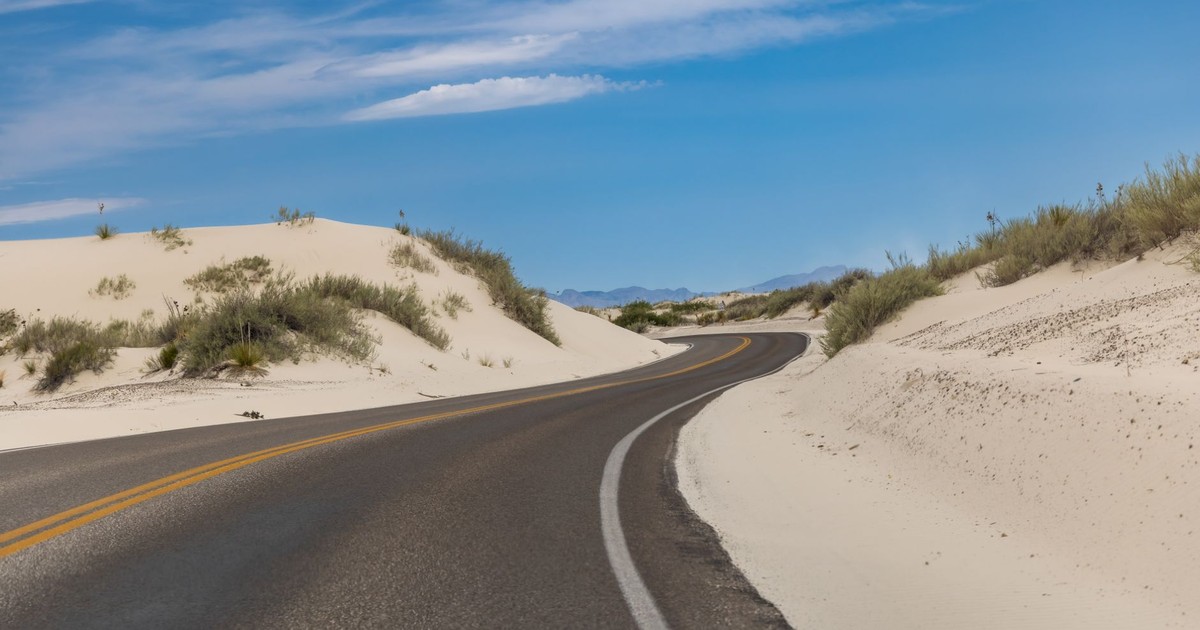 A winding road cuts through the white sand dunes of New Mexico under a vibrant blue sky.