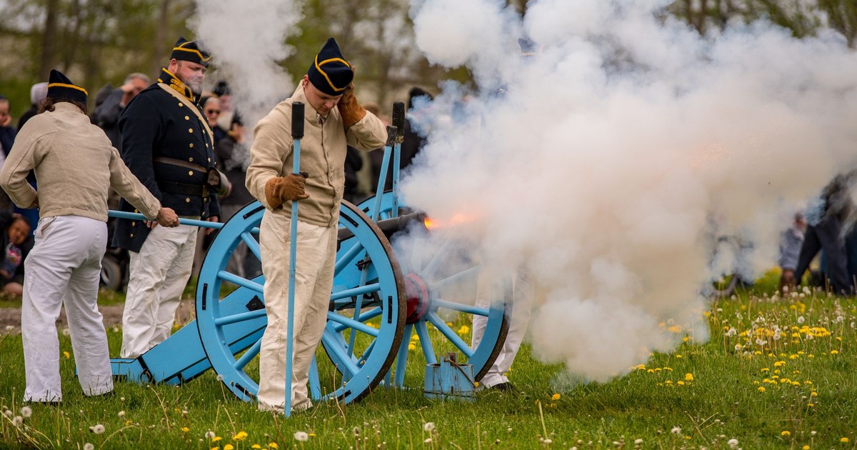 Civil war reenactors fire a cannon, creating a cloud of smoke on a grassy field.
