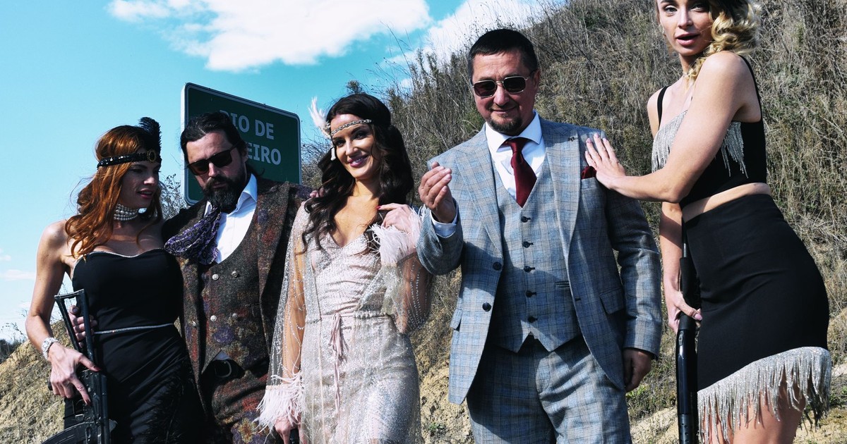 Five adults dressed in Gatsby-era gangster costumes outdoors, showcasing vintage style.