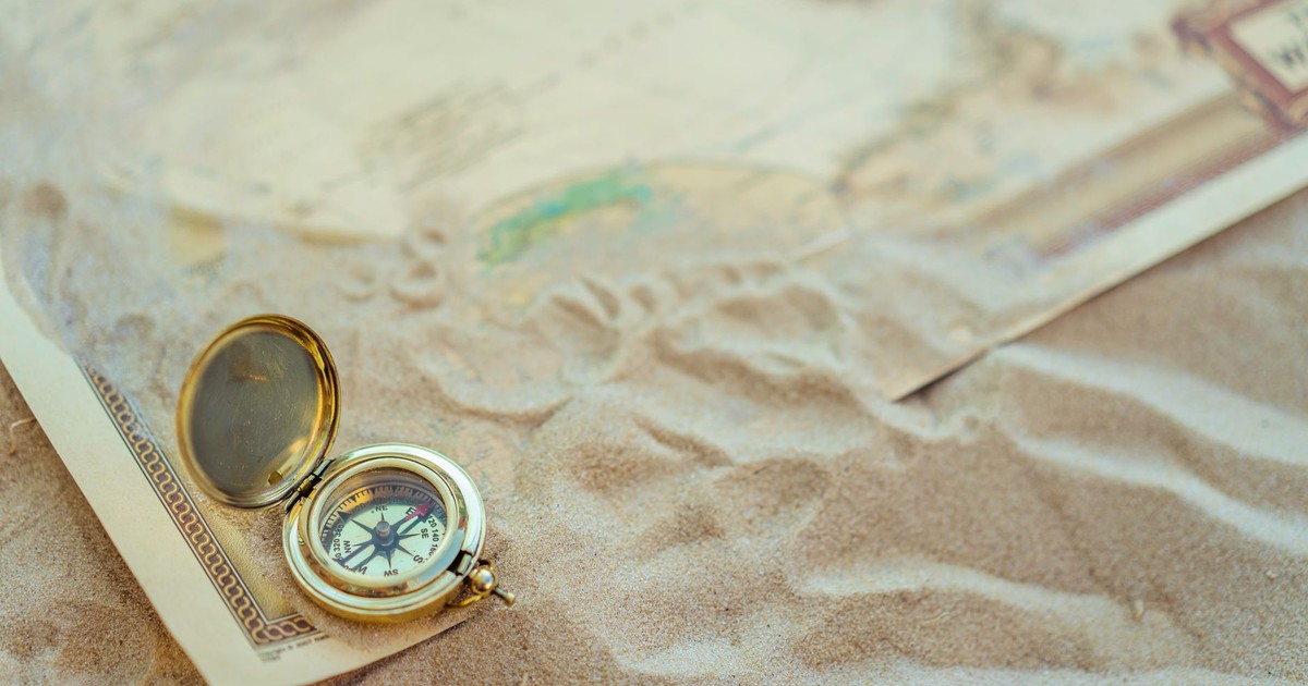A close-up of a vintage compass on sand with a map, symbolizing travel and exploration.
