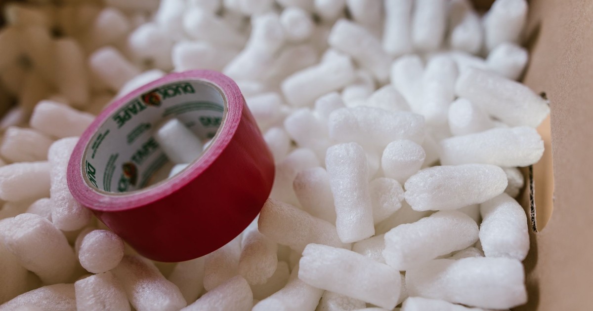Close-up of red duct tape on packing peanuts in a cardboard box for shipping or moving.