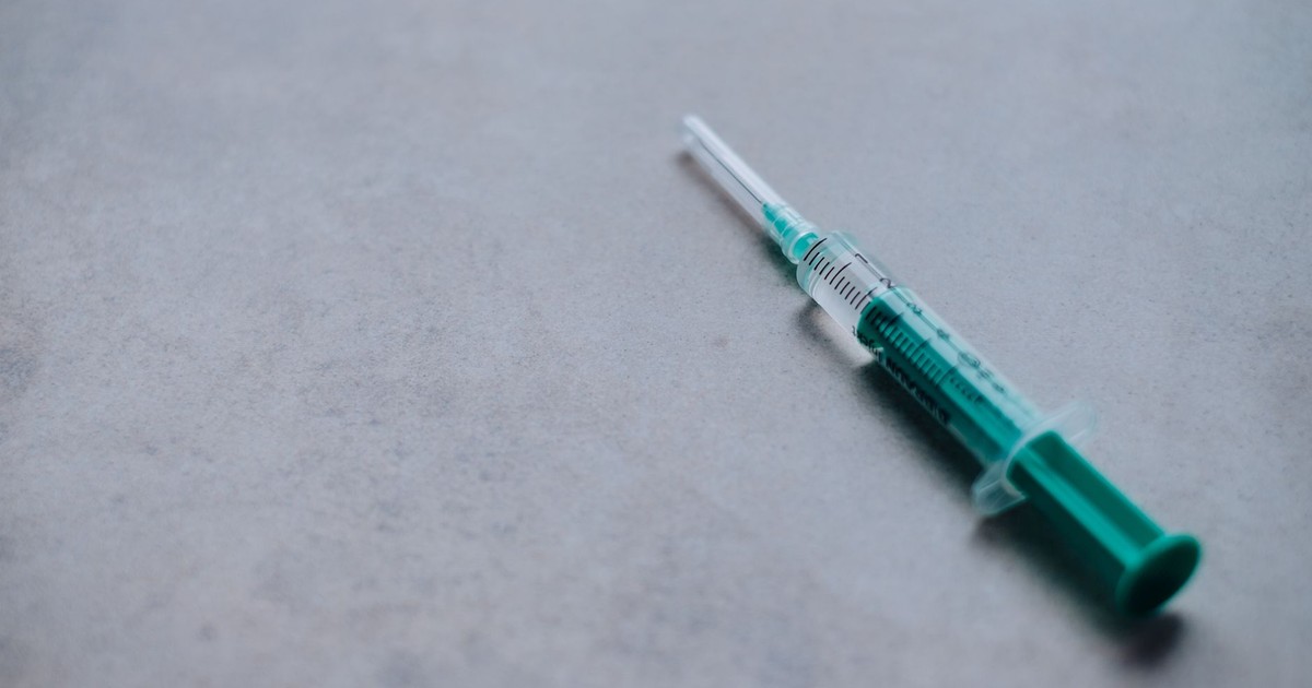 Close-up of a green syringe on a gray surface, ideal for health and medical themes.