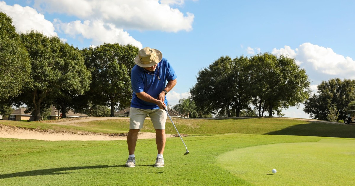 An adult male golfer putting on a lush golf course in Eustis, Florida under a bright sky.