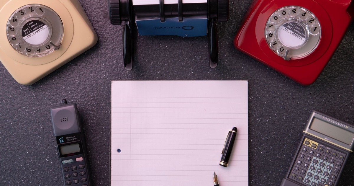 Vintage office equipment with rotary phones, notebook, and calculator flat lay composition.