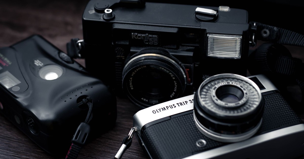 A set of vintage cameras including Olympus and Konica models on a wooden surface.