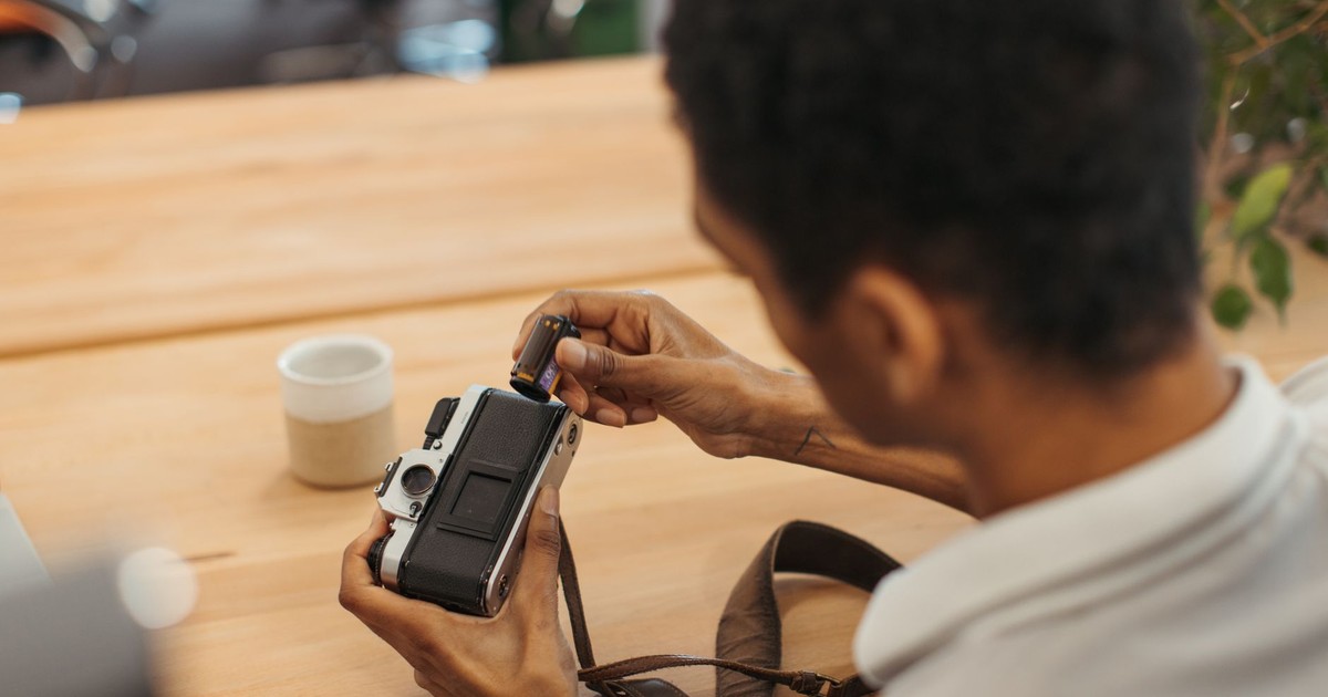 Person loading a roll of film into a vintage camera, focused with hands visible.