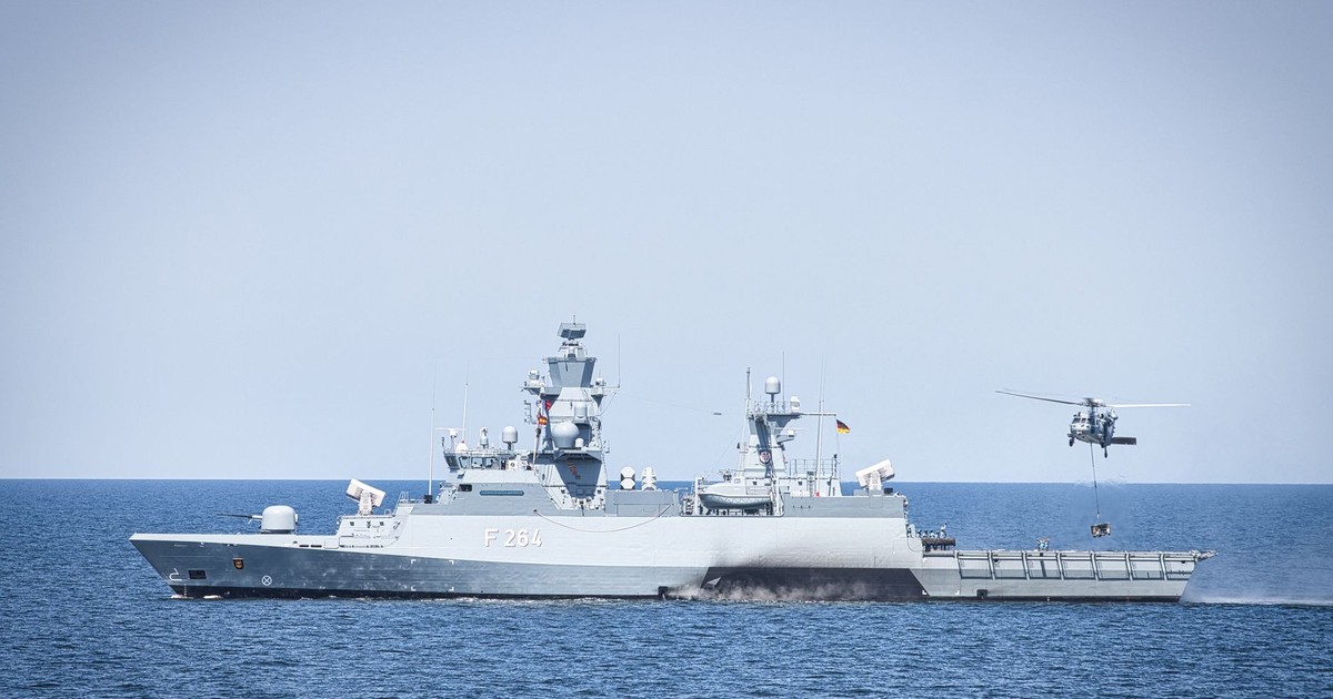 A naval frigate navigates open waters with a hovering helicopter, showcasing maritime operations.