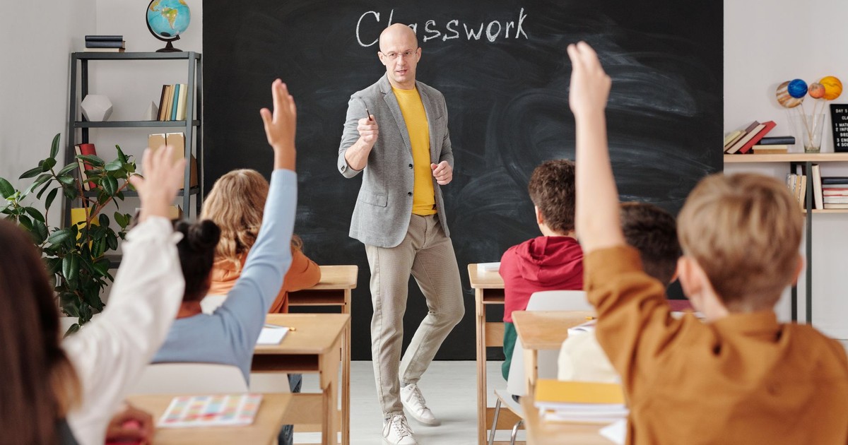 Teacher interacting with students raising hands in a classroom setting.