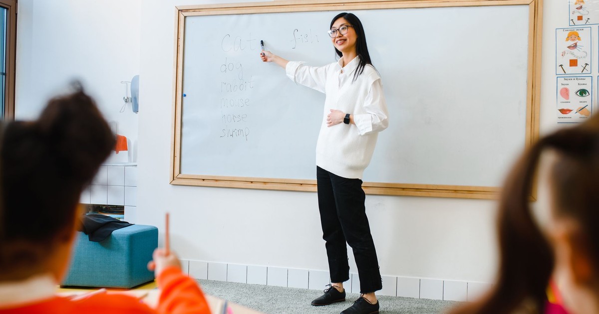 Smiling teacher instructing students in a classroom setting using a whiteboard.