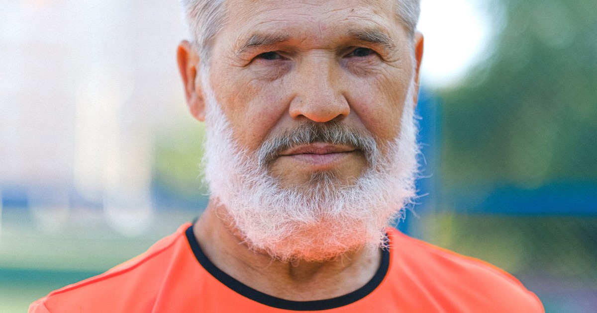 Crop senior male with gray hair and beard in casual t shirt standing in nature and looking at camera