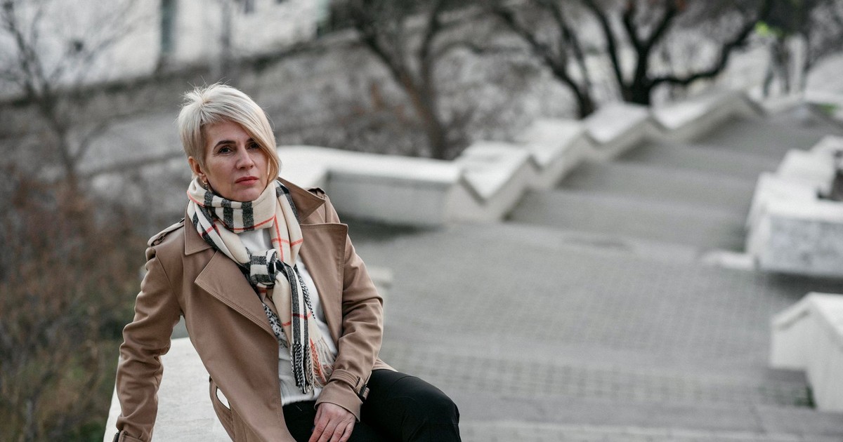 Blonde woman in a trench coat posing on an outdoor staircase, showcasing urban fashion.