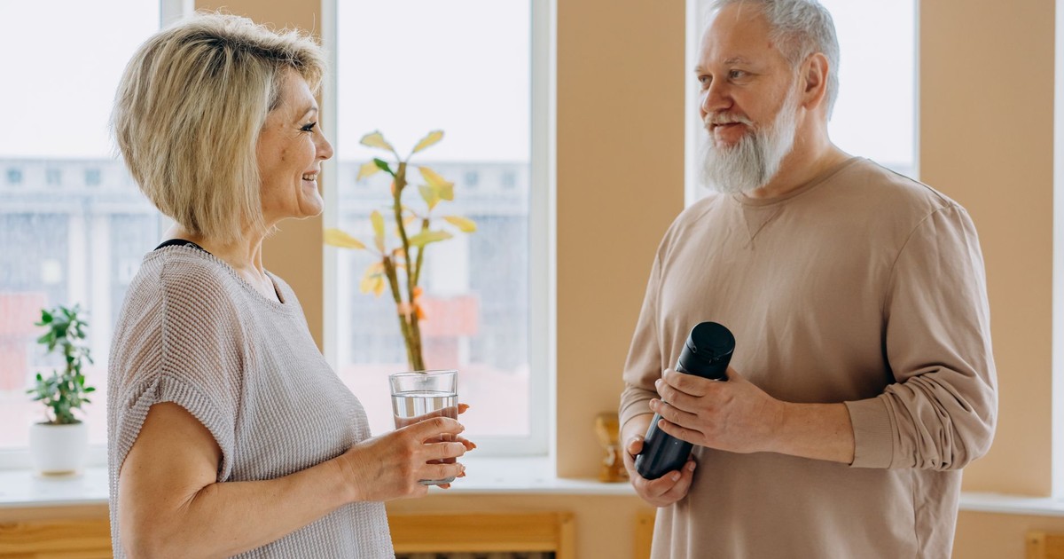 Elderly couple smiling and talking indoors, promoting a healthy lifestyle.