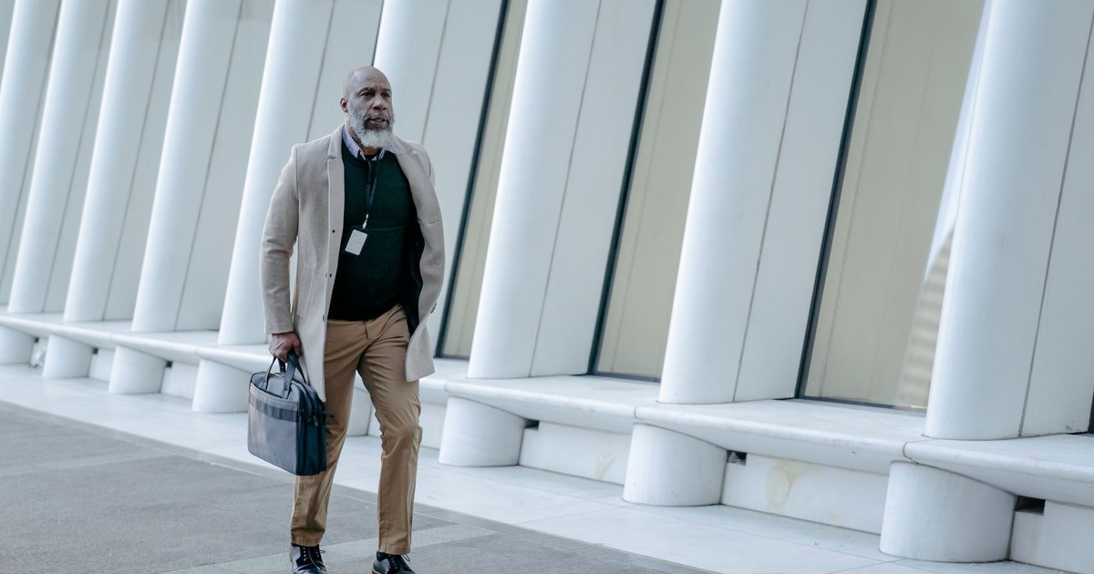 A mature man in business attire walking by contemporary white pillars in a cityscape.