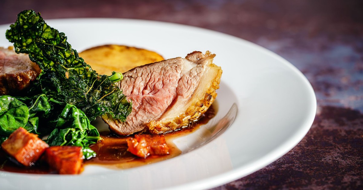 Savor a gourmet duck breast dish with crispy kale and a rich sauce, exquisitely presented on a white plate.