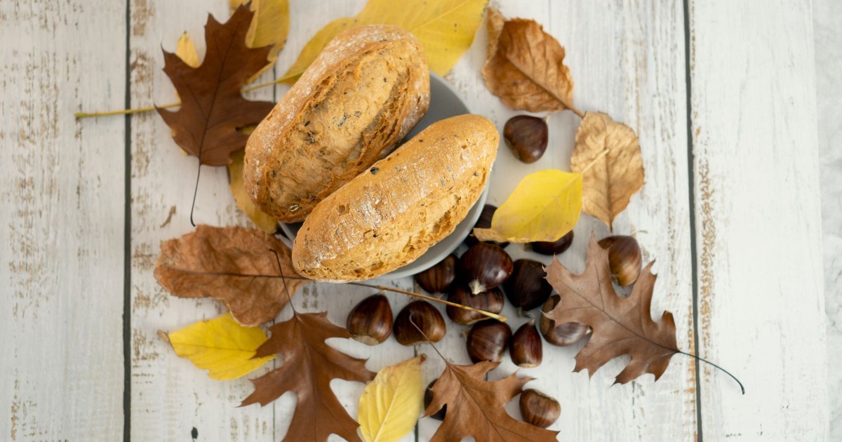 A cozy autumn scene with freshly baked bread, chestnuts, and colorful leaves on a rustic wood table.